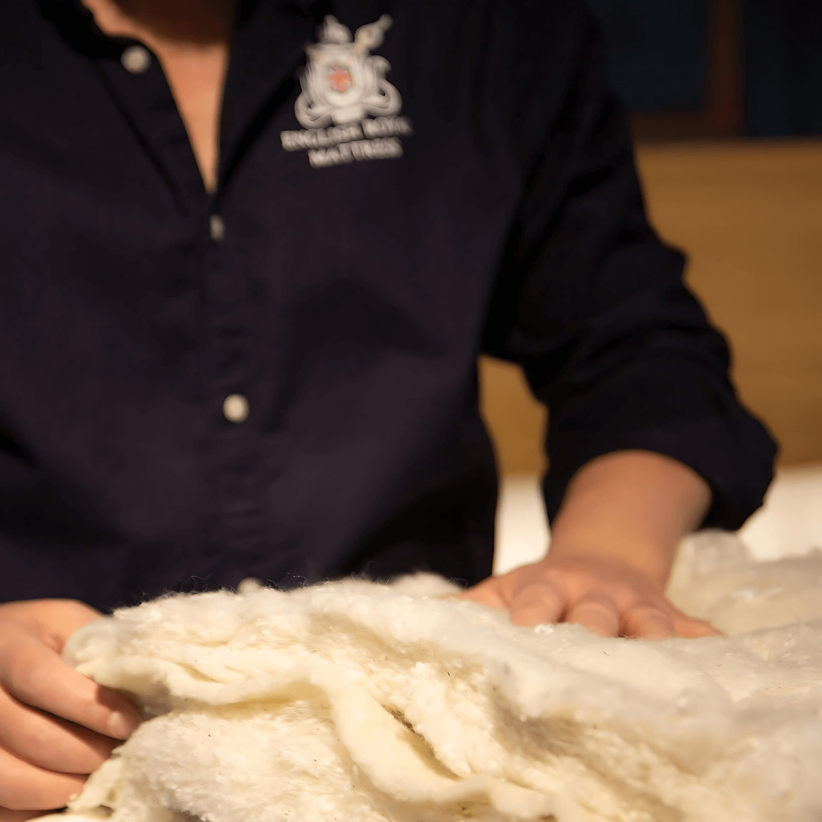 Handcrafted natural British mattress materials being inspected by a craftsman in dark blue uniform.